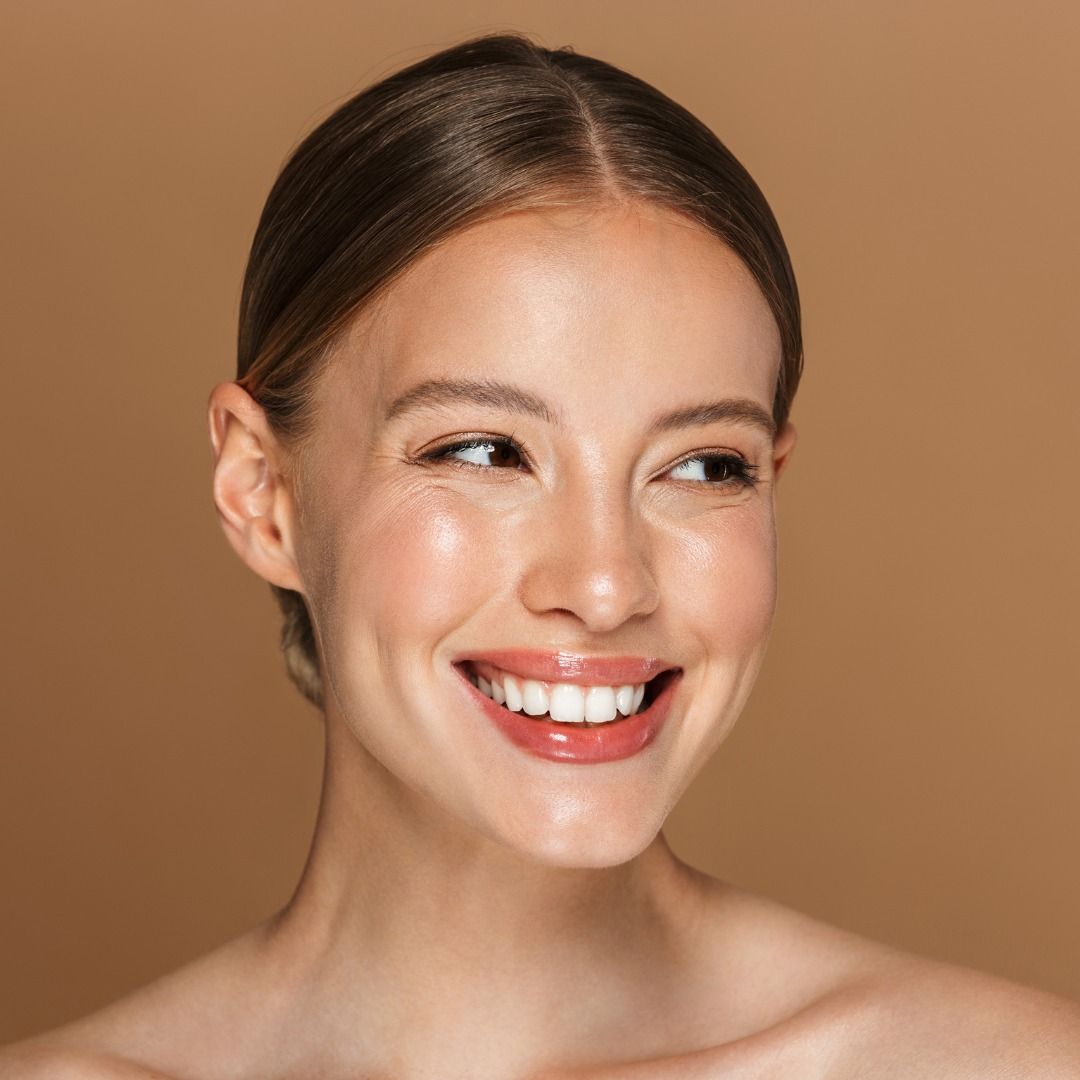 Smiling woman with glowing skin against neutral background.