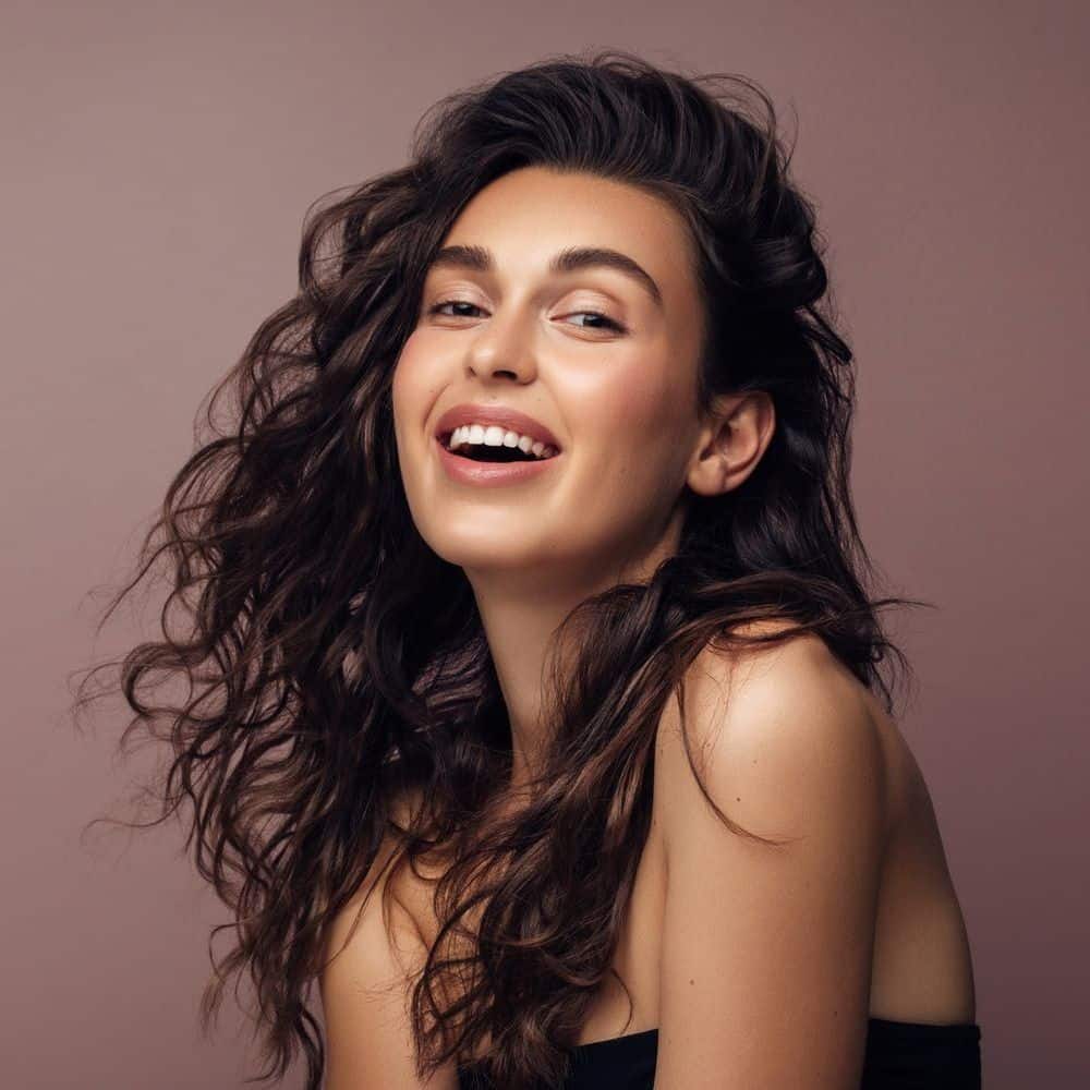 Smiling woman with curly hair against brown background.