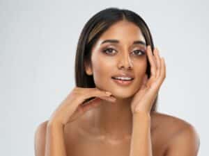 Beautiful young woman happily touching her face after getting Sculptra or dermal filler injections for a balanced look.
